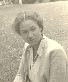 A vintage black‑and‑white photograph showing a person outdoors on grass, wearing a light‑colored collared shirt and jacket. The image has a soft, aged appearance with natural lighting and a shallow depth of field.
